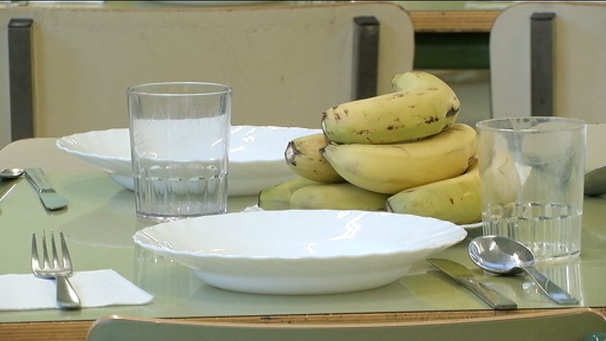 Mesa puesta en un comedor escolar con plátanos de postre