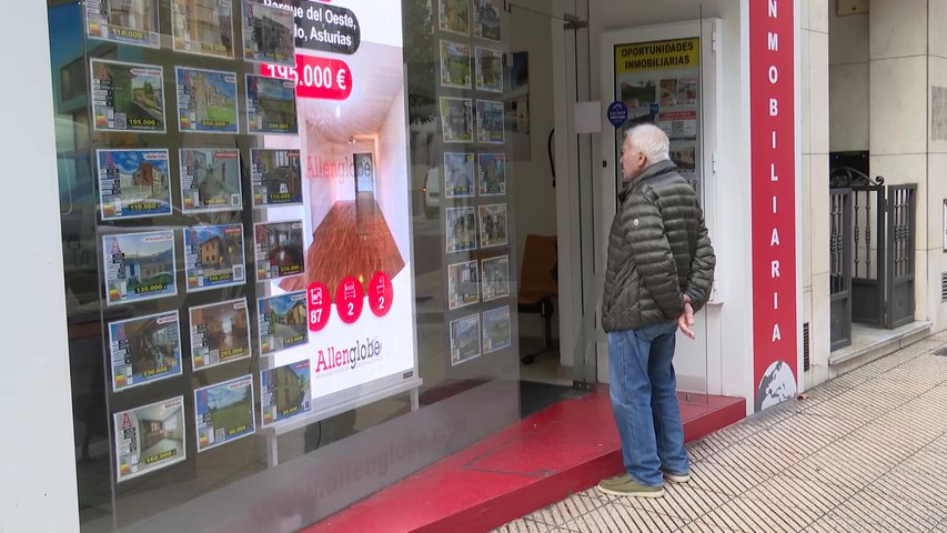 Un señor mayor mira precios en los carteles colgados en el escaparate de una inmobiliaria